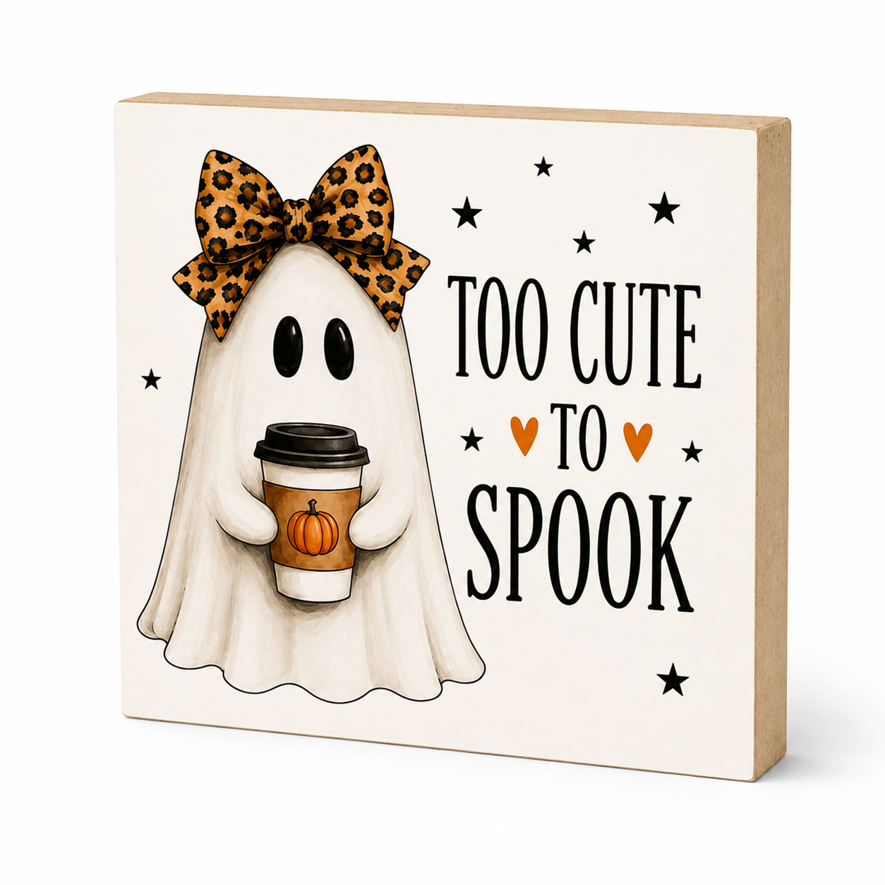 A square decorative sign with a light wood border and cream face, featuring an illustrated ghost in a leopard-print bow holding a coffee cup, next to the text 'TOO CUTE TO SPOOK' with small orange hearts and black stars.