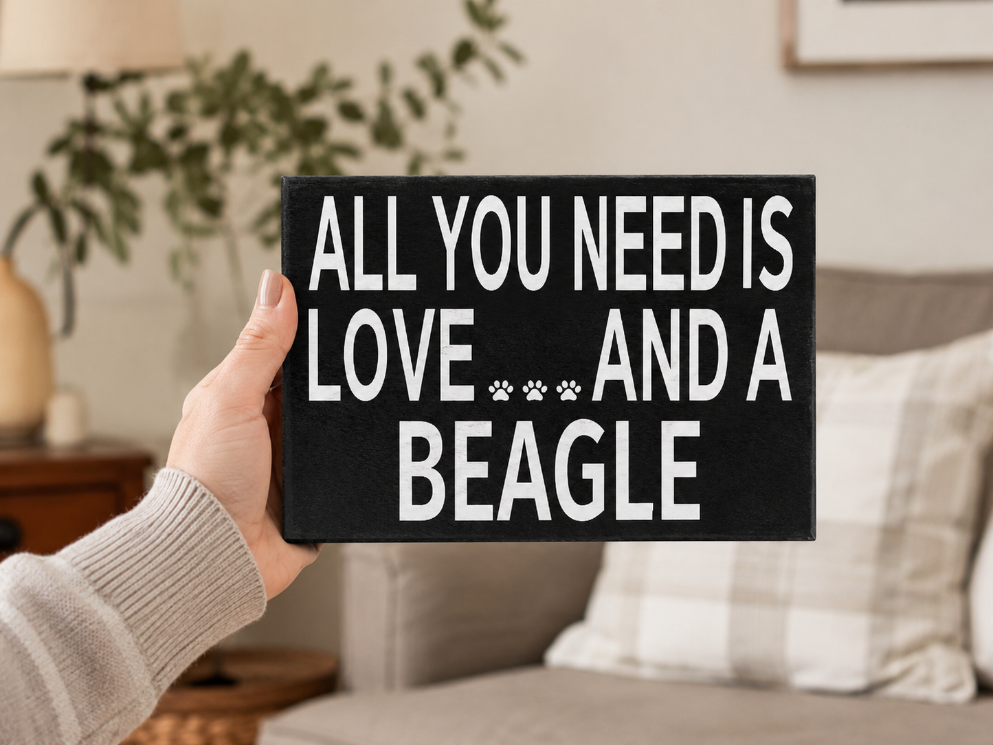 A hand holding a black rectangular sign with white text that reads 'ALL YOU NEED IS LOVE.
