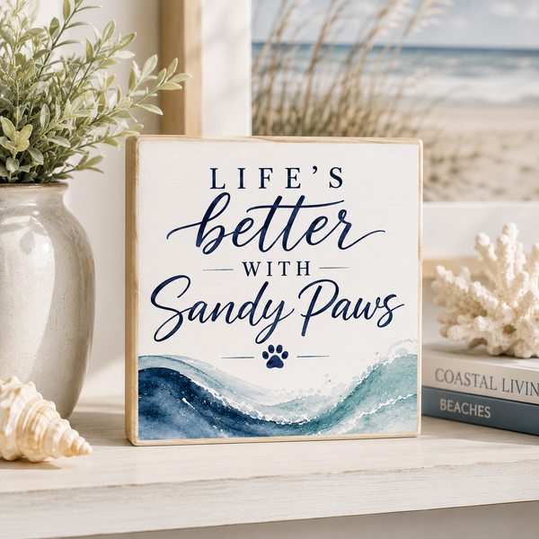 Decorative sign with 'Life's better with sandy paws' text on a shelf with decorative items.