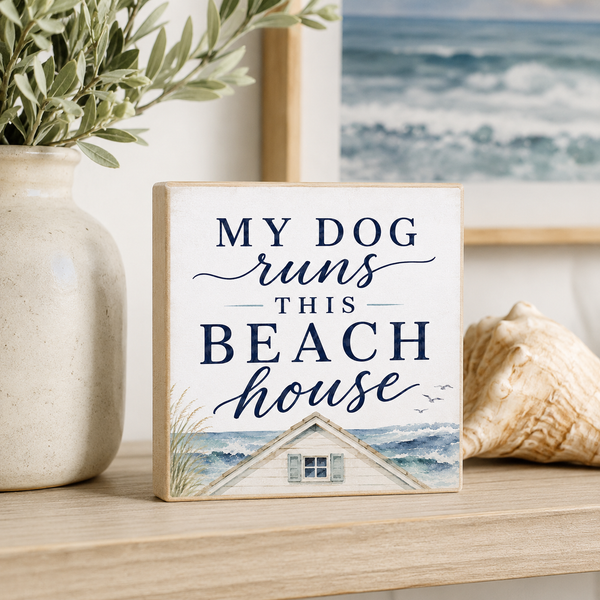 Decorative sign with 'My dog runs this beach house' text on a shelf with decorative items.