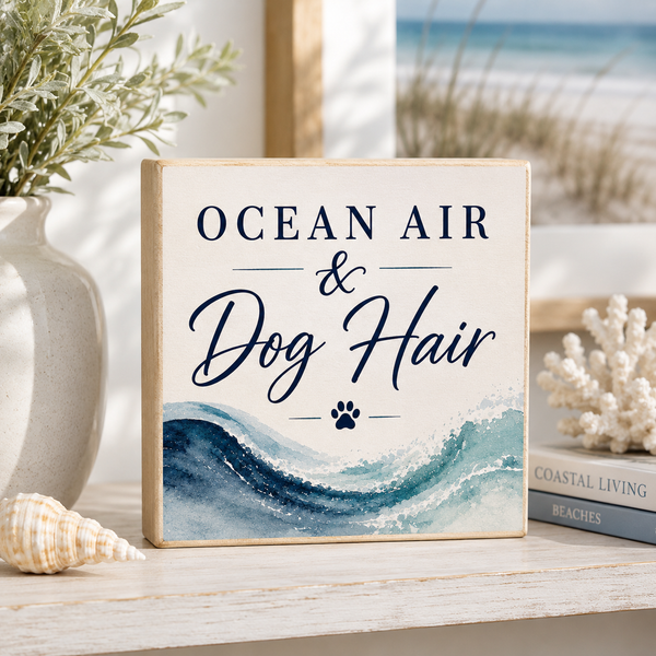 Decorative sign with 'Ocean Air & Dog Hair' text on a shelf with decorative items.