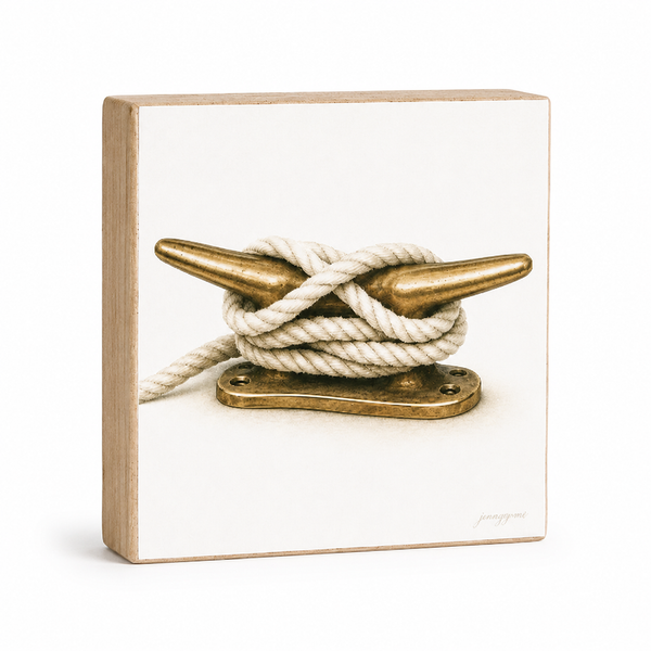 A square decorative wall plaque featuring a printed photograph of a white rope tied around a brass nautical cleat, with a light natural wood border on a white background.