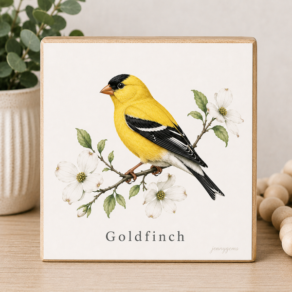 Framed artwork of a goldfinch on a branch with white flowers and leaves.