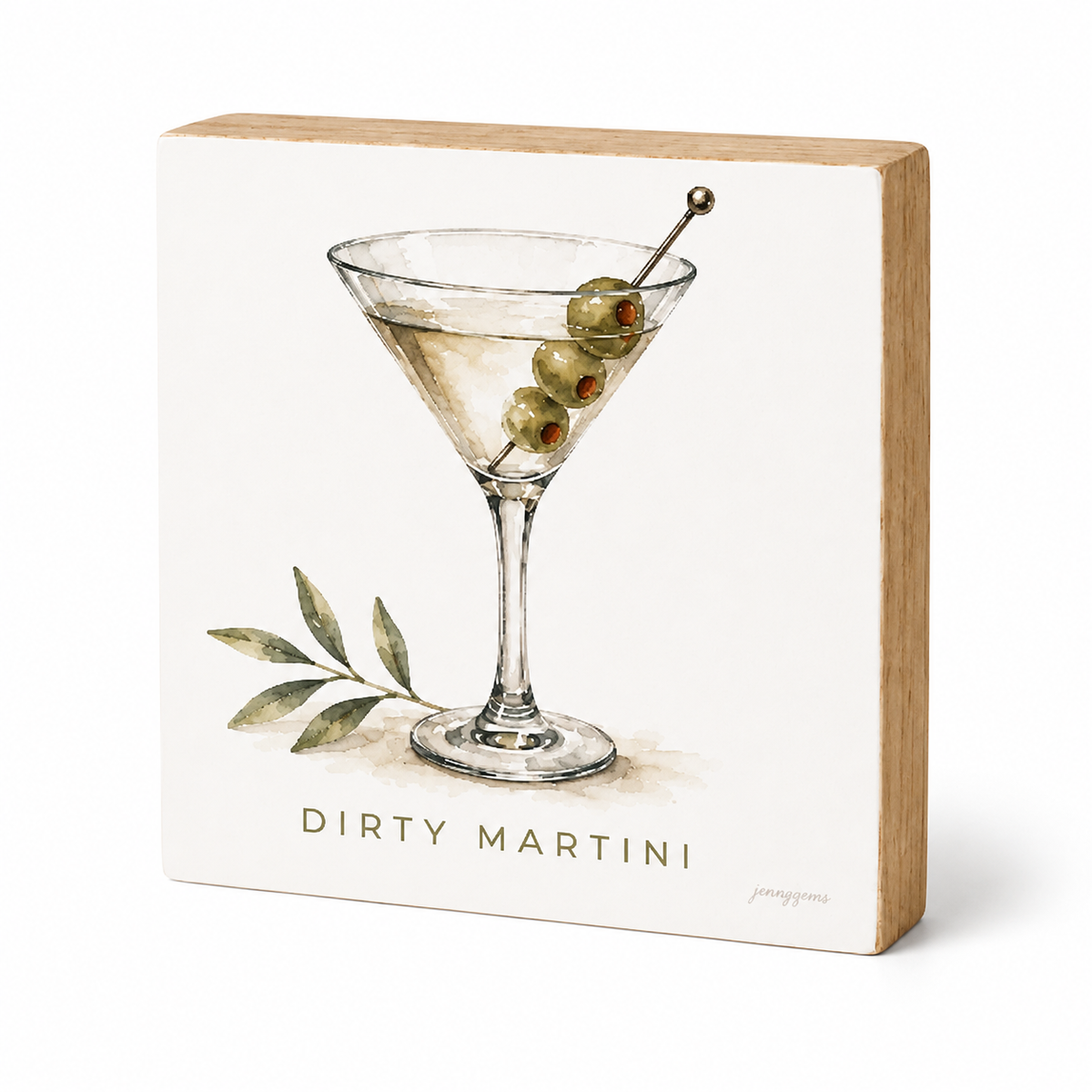 A square decorative block sign with a light wood edge and a white front panel featuring an illustration of a martini glass with green olives, a leaf sprig, and the text 'DIRTY MARTINI'.