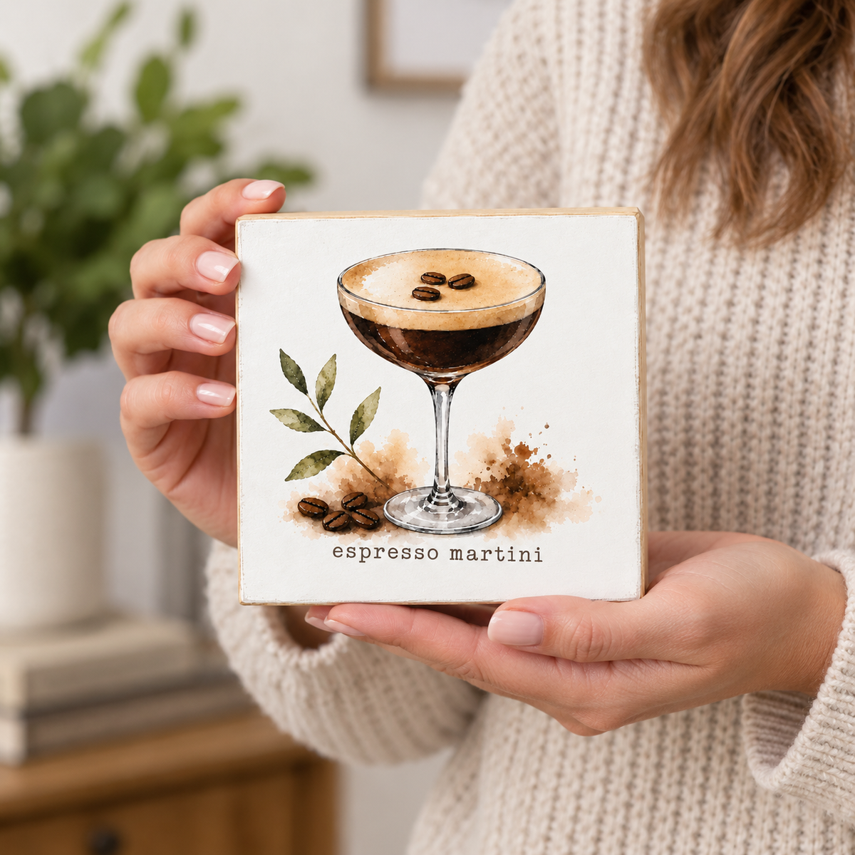 A person in a cream knit sweater holds a square ceramic tile featuring a watercolor-style espresso martini illustration with the text 'espresso martini' below.