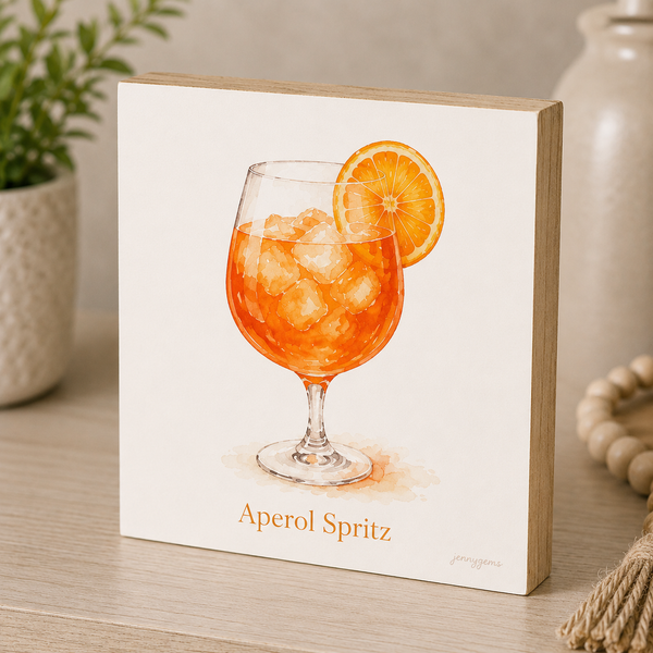 Framed artwork of an Aperol Spritz cocktail with an orange slice on a wooden surface.