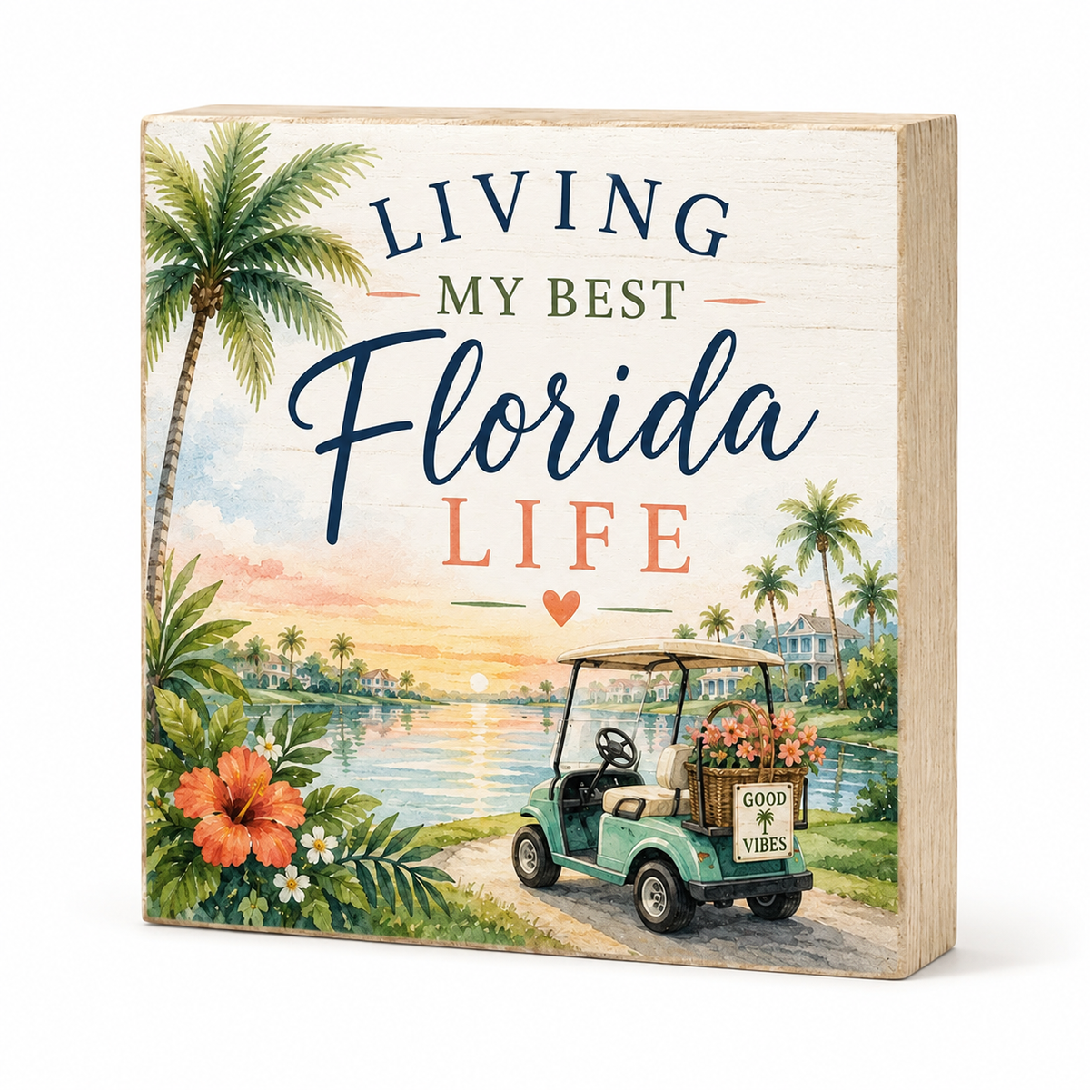 A square decorative wooden block sign with a Florida-themed illustration and the text 'LIVING MY BEST Florida LIFE.' The design shows palm trees, a sunset over water, flowers, and a golf cart on a path.