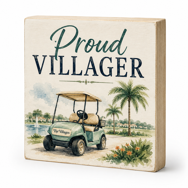 A square decorative wooden sign with a light natural wood frame and a printed tropical scene. The sign reads 'Proud VILLLAGER' in large lettering above an illustration of a golf cart, palm trees, water, and flowers.
