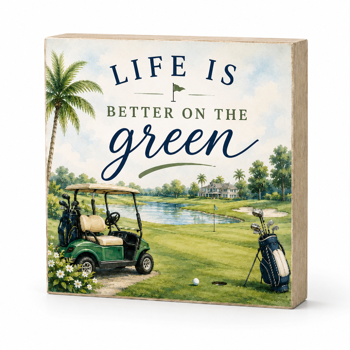A square decorative wooden block sign featuring a golf course scene with the text 'LIFE IS BETTER ON THE green' in navy and green lettering. The illustration includes a palm tree, a green golf cart, a golf bag, a golf ball, and a lake in the background.