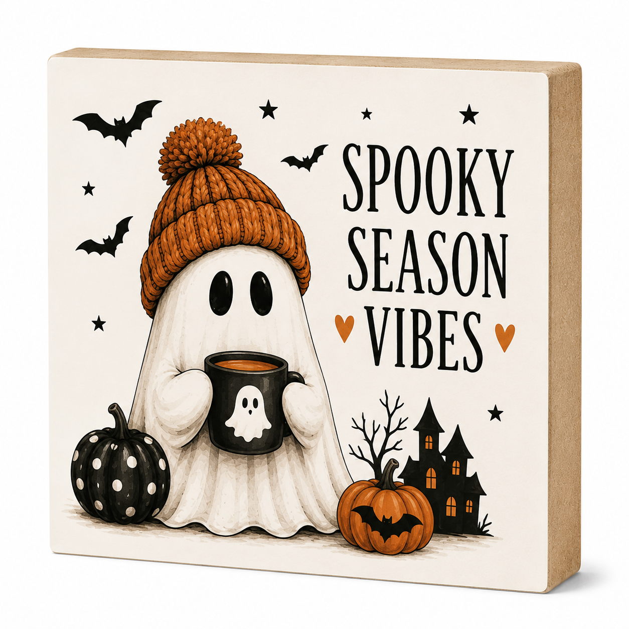 A square decorative block sign with a Halloween design that reads 'SPOOKY SEASON VIBES.' The front shows a ghost in an orange knit hat holding a black mug, with bats, stars, a pumpkin, haunted house, and small hearts on an off-white background.