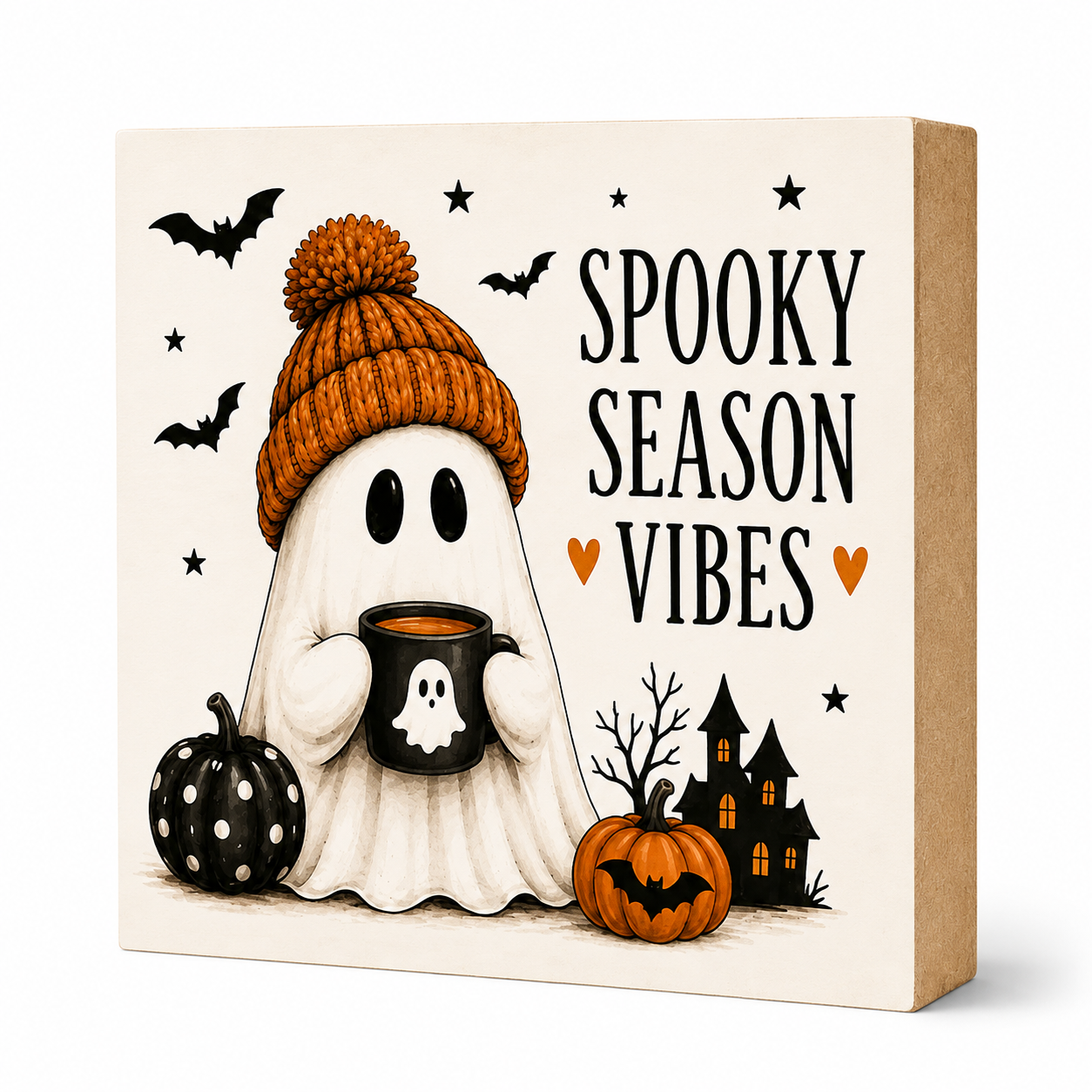 A square decorative sign with a kraft paper side and a cream front panel featuring a Halloween illustration. The design shows a ghost in an orange knit hat holding a black mug, with a black polka-dot pumpkin, a real orange jack-o'-lantern, a haunted house, bats, stars, and the text 'SPOOKY SEASON VIBES'.