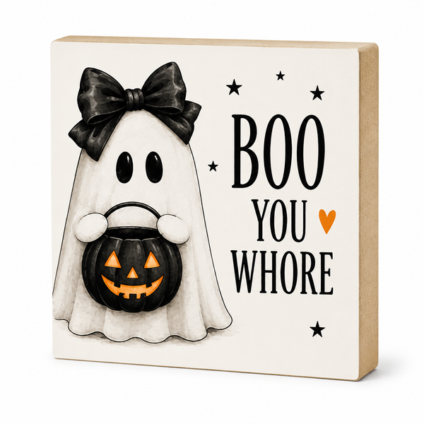 A square decorative sign with a Halloween theme, featuring a cartoon ghost in a black bow holding a jack-o'-lantern bucket, next to the text 'BOO YOU WHORE' with small black stars and an orange heart on a cream background, with a natural wood side edge.