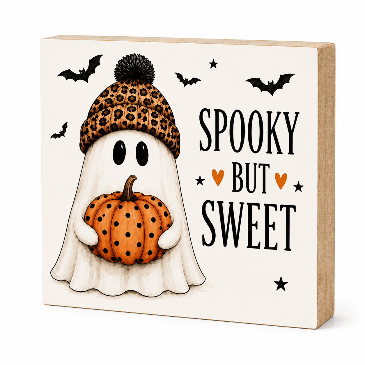 A square wooden decorative block sign with a cream front panel and natural wood sides. The front features an illustrated ghost wearing a leopard-print beanie and holding an orange pumpkin, with black bats, stars, and the words “SPOOKY BUT SWEET” on a white background.
