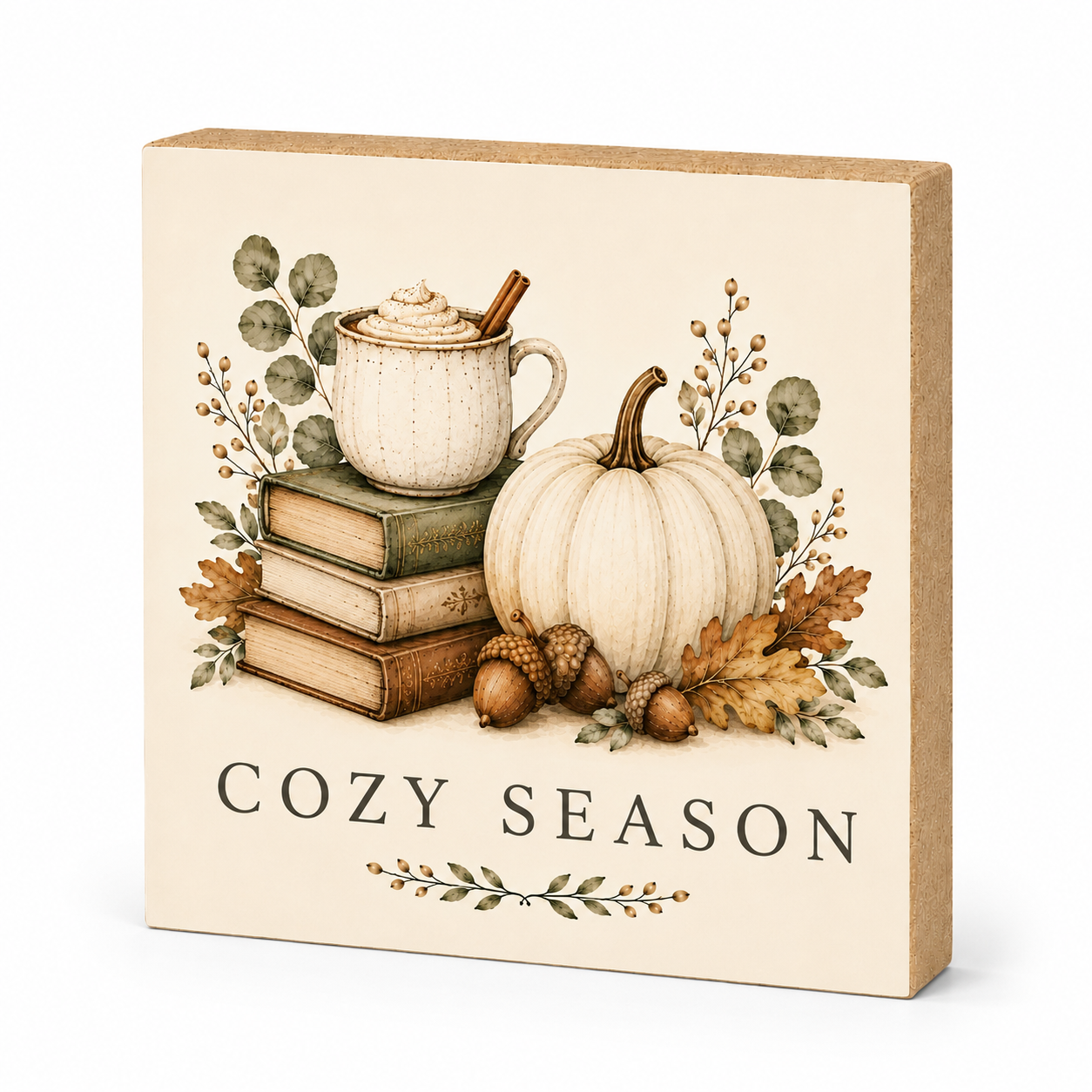 A square decorative sign with a kraft-paper border and a cream face, featuring an autumn illustration of a mug on stacked books, a white pumpkin, acorns, leaves, and the words “COZY SEASON.”.