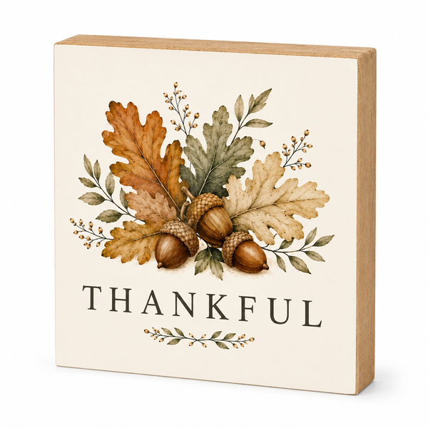 A square decorative wooden sign with a light natural wood border and a cream face, featuring an autumn leaf and acorn illustration above the word 'THANKFUL' in dark serif lettering.