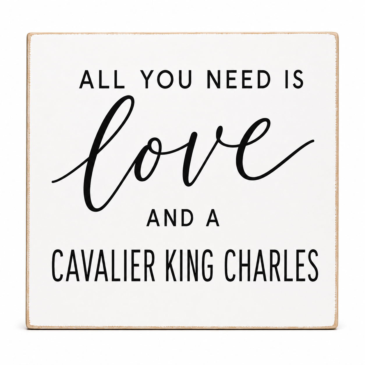 A square white decorative sign with a light natural wood border, featuring the text 'ALL YOU NEED IS love AND A CAVALIER KING CHARLES' in black lettering, shown on a plain white background.