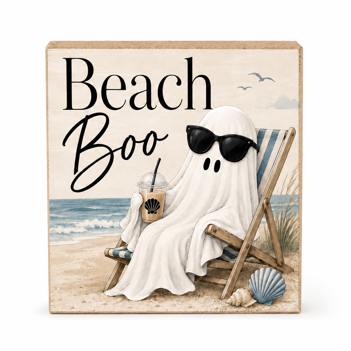 Square decorative sign with a beach scene and the words “Beach Boo” in black lettering. The sign shows a ghost-like figure draped in a white sheet sitting in a beach chair on the sand, wearing black sunglasses and holding an iced coffee, with blue ocean, seashells, and a few birds in the background.
