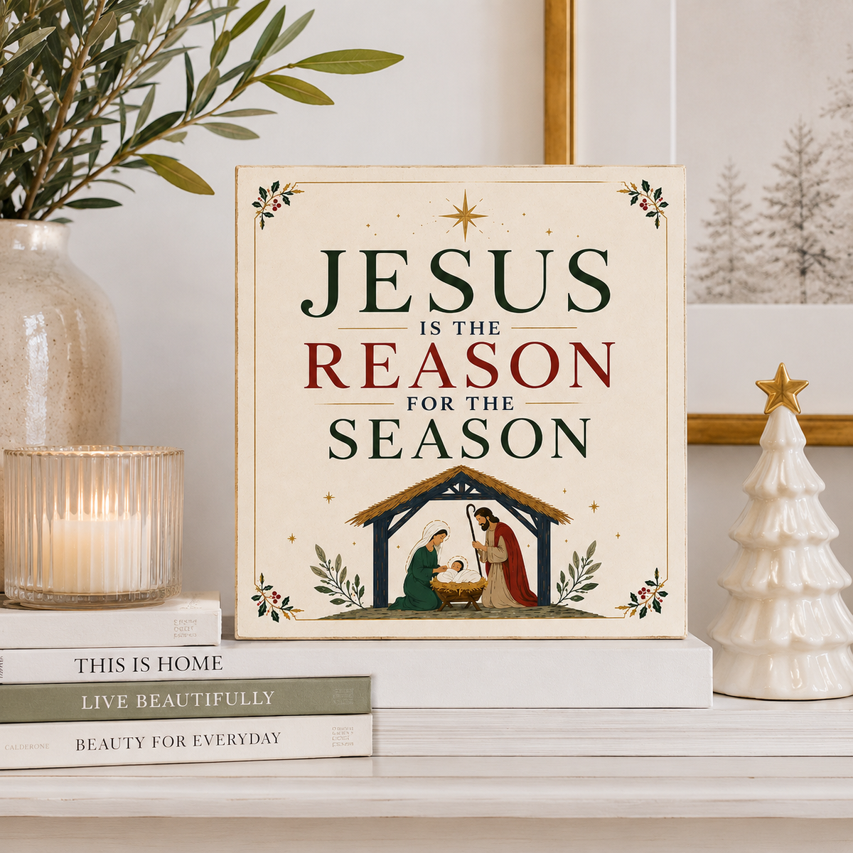 A square decorative sign with a nativity illustration and the text 'JESUS IS THE REASON FOR THE SEASON' is displayed on a shelf in a styled home setting with books, a candle, a plant, and a small white Christmas tree.