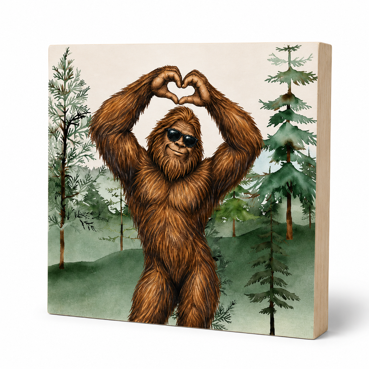 A square wooden block print featuring a cartoon-style brown furry figure making a heart with its hands, set against a forest background with green trees and hills. The print is shown at an angle to display the thickness of the wooden block on a white background.
