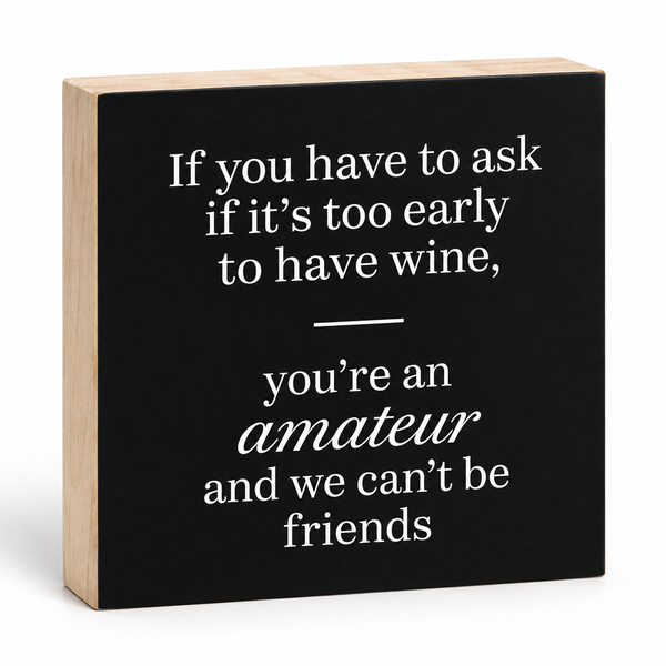 A square decorative block sign with a black front panel and natural wood sides, printed with the quote: 'If you have to ask if it's too early to have wine, you're an amateur and we can't be friends' in white text.