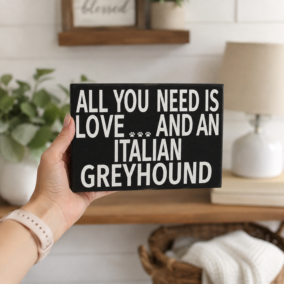 A hand holds a black rectangular sign with white text that reads 'ALL YOU NEED IS LOVE.