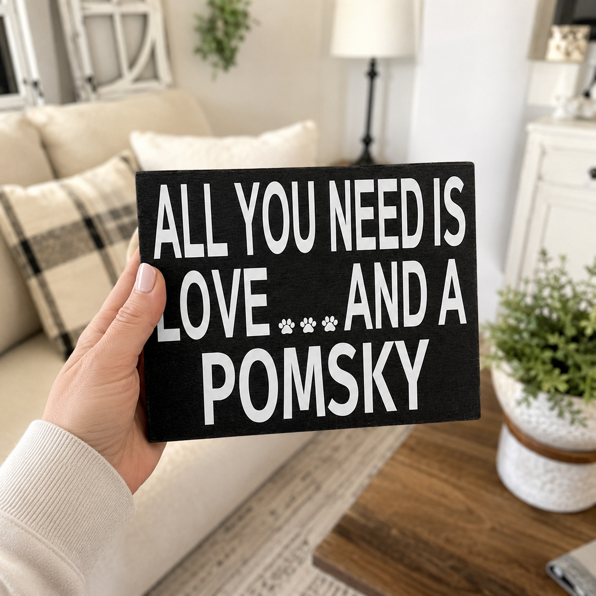 A hand holding a black rectangular wooden sign with white text that reads 'ALL YOU NEED IS LOVE.