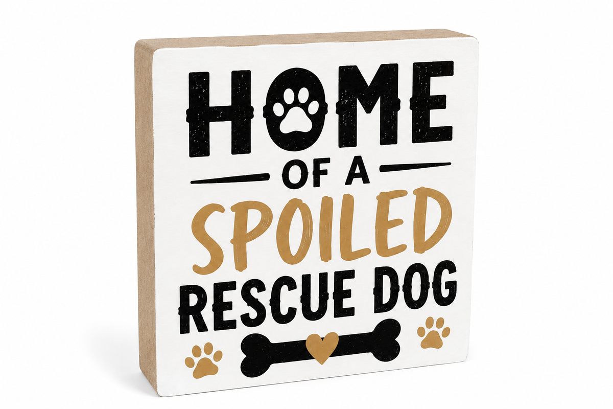 A square decorative wooden sign with a white front and natural wood sides, printed with the phrase 'HOME OF A SPOILED RESCUE DOG' in black and tan lettering, with paw prints and a bone graphic, on a white background.