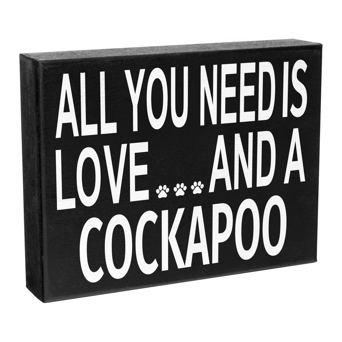 A black and white wooden sign with the text 'All You Need Is Love and a Cockapoo' and a paw print symbol.