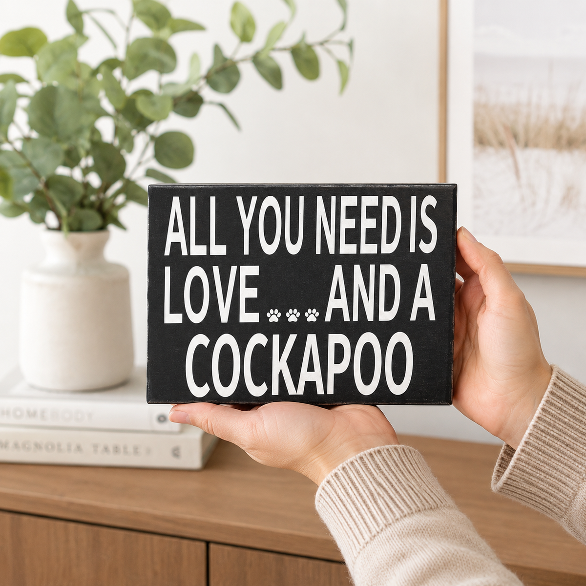 A person holds a black rectangular sign with white text that reads 'ALL YOU NEED IS LOVE.