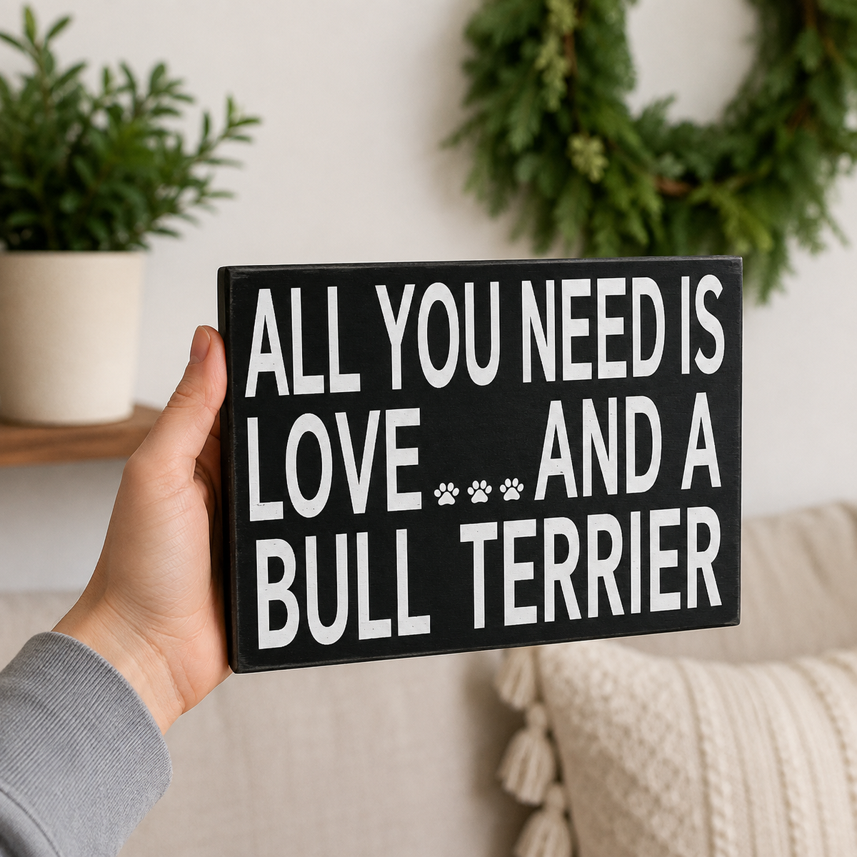 A hand holding a rectangular black sign with bold white text that reads 'ALL YOU NEED IS LOVE.