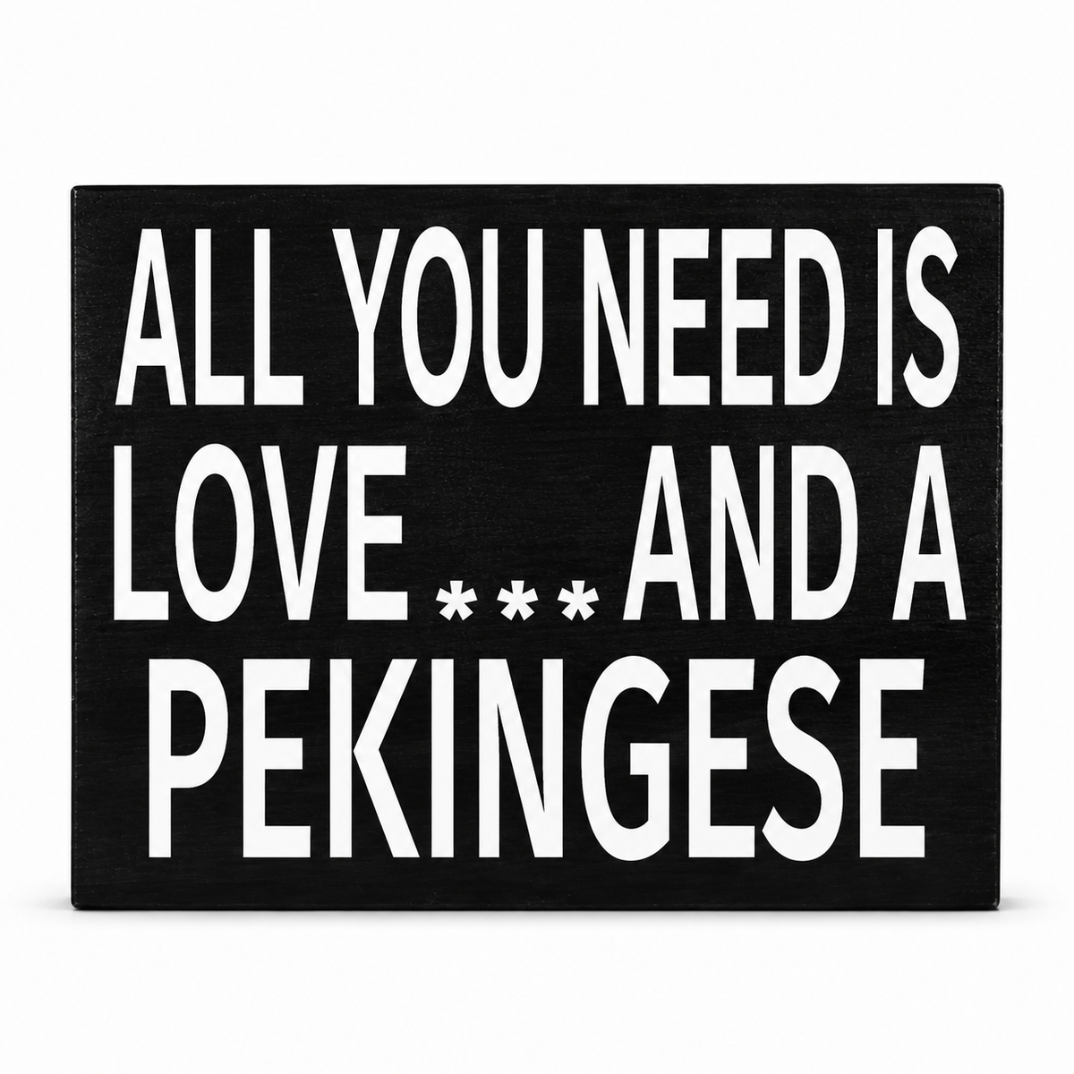 A rectangular black sign with bold white text reading 'ALL YOU NEED IS LOVE *** AND A PEKINGESE' on a plain white background.