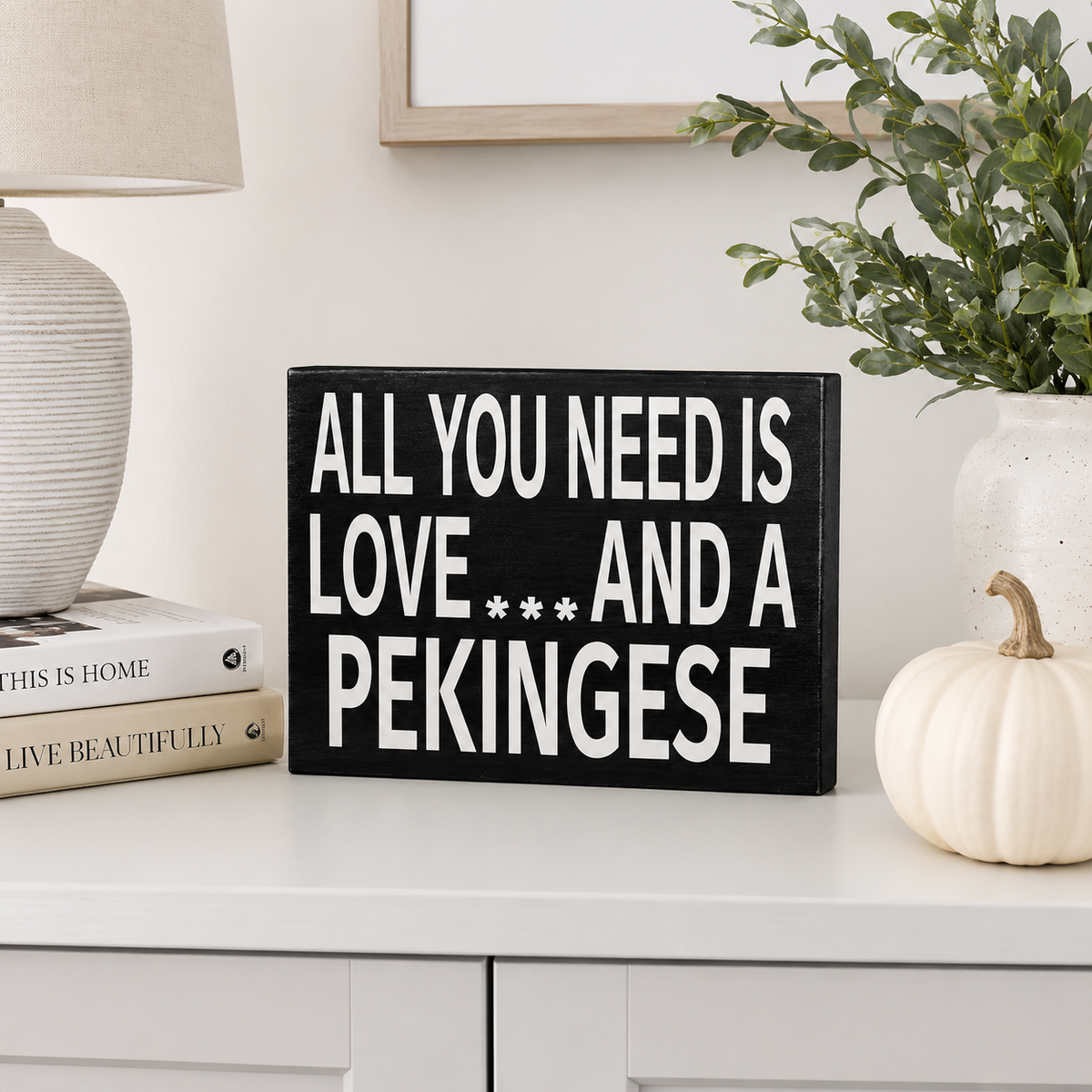 A rectangular black wooden sign with white text reading 'ALL YOU NEED IS LOVE.
