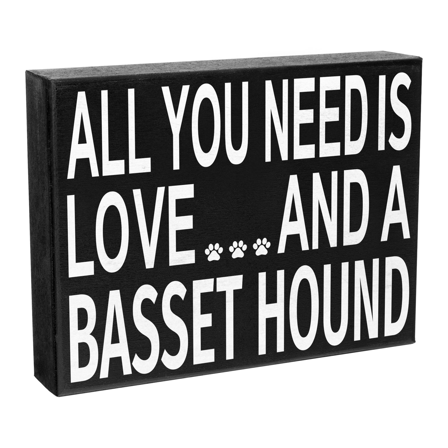 A wooden box sign with the text 'All You Need is Love and a Basset Hound' and a paw print symbol, predominantly in black color.
