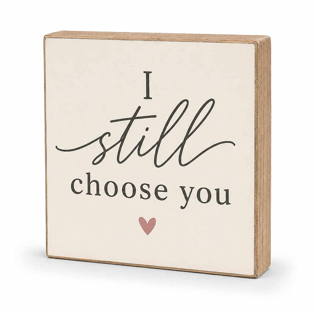 A square wooden sign with a cream face and natural wood edges, printed with the phrase 'I still choose you' in black script and serif text, plus a small dusty pink heart below.