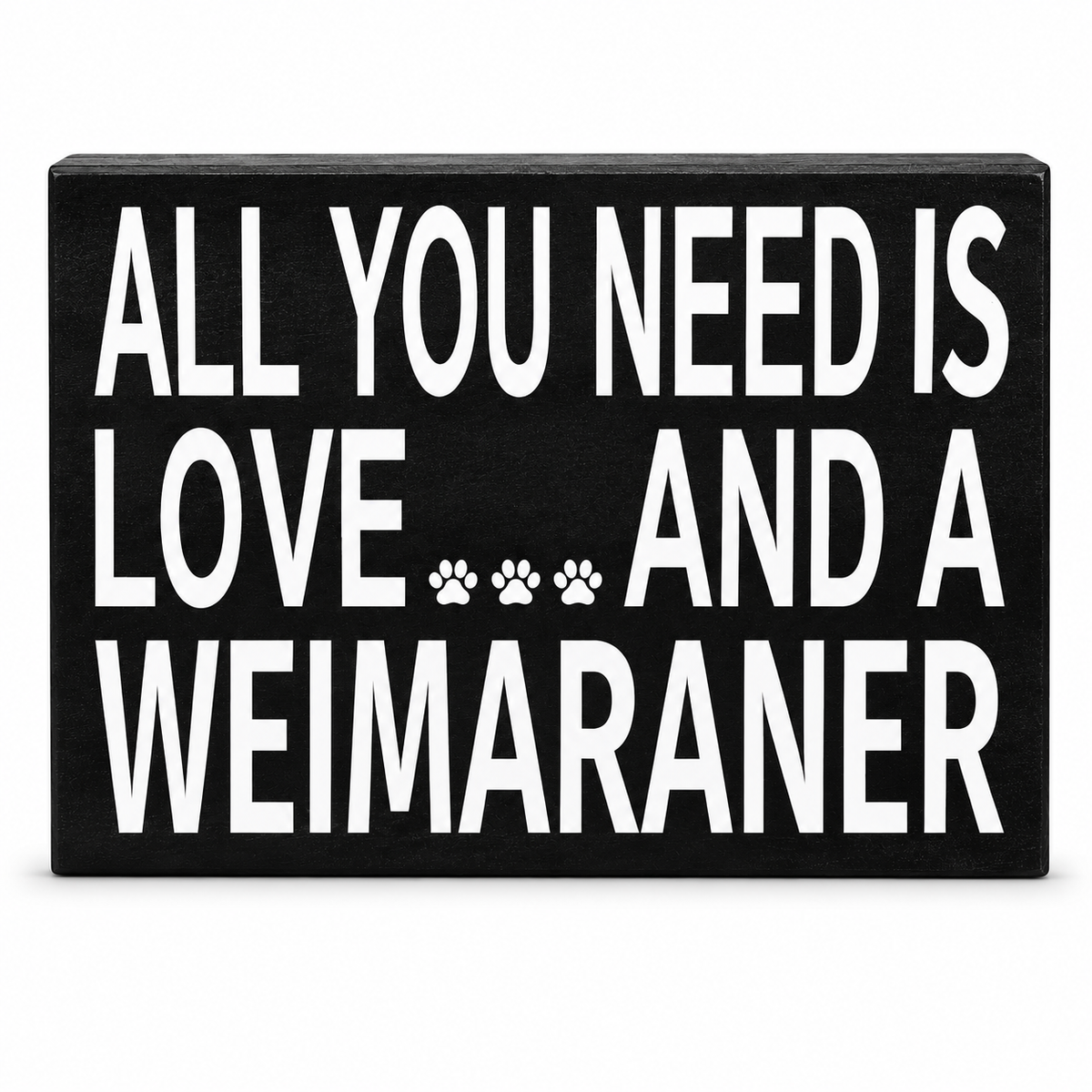 A rectangular black decorative sign with bold white text reading 'ALL YOU NEED IS LOVE.