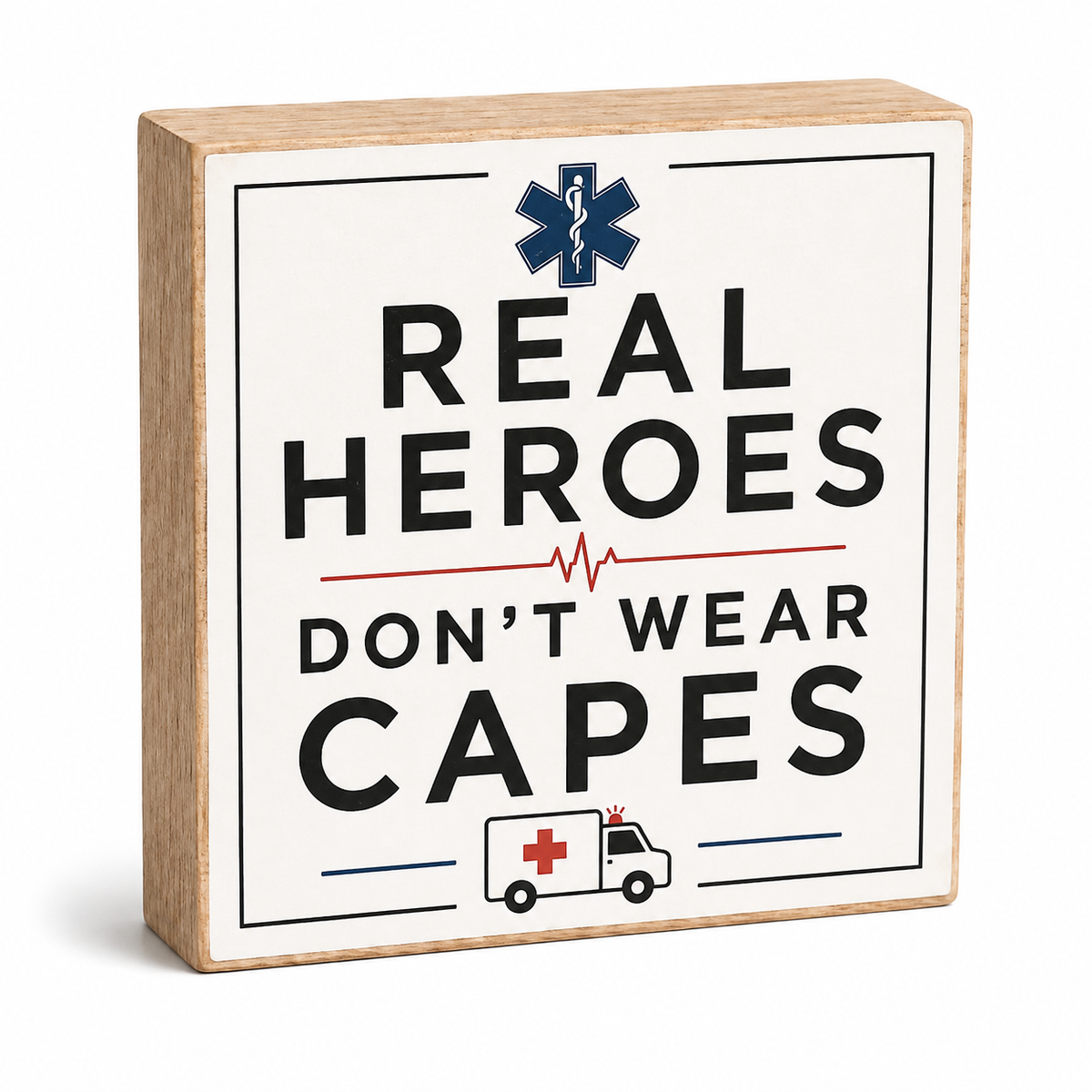 A square wooden sign with a light natural wood border and a white face. The sign features the text 'REAL HEROES DON'T WEAR CAPES' in bold black lettering, with a blue Star of Life symbol at the top and a small ambulance illustration at the bottom.