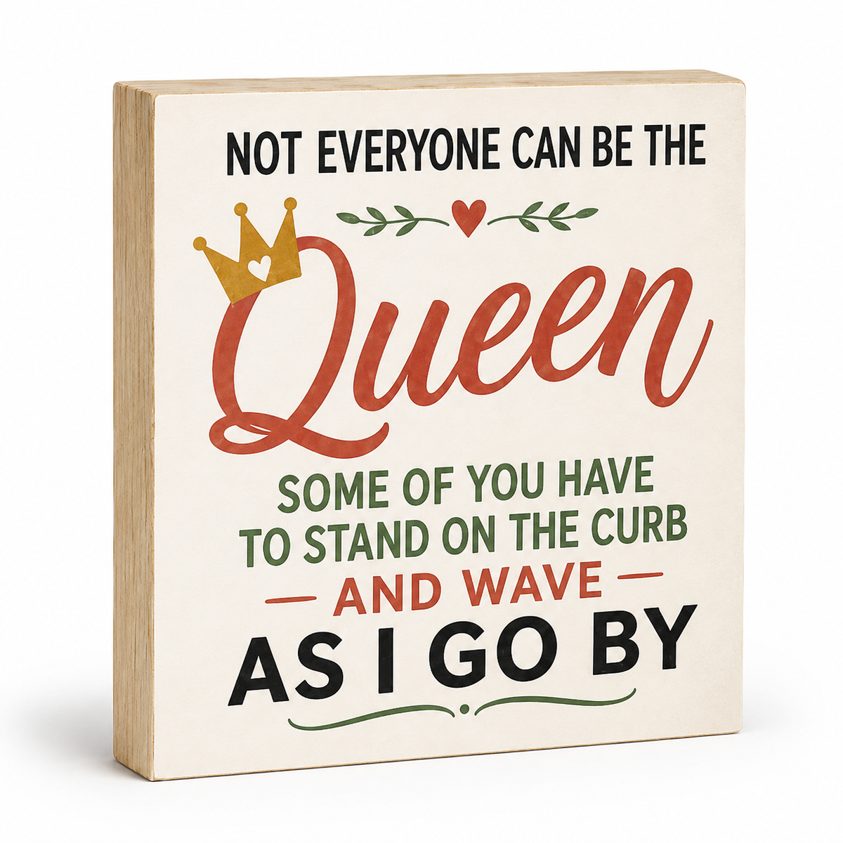A square decorative wooden sign with a light natural wood edge and a cream face, printed with the quote 'NOT EVERYONE CAN BE THE Queen SOME OF YOU HAVE TO STAND ON THE CURB AND WAVE AS I GO BY' in black, rust red, and green lettering, with a small gold crown and heart graphic.
