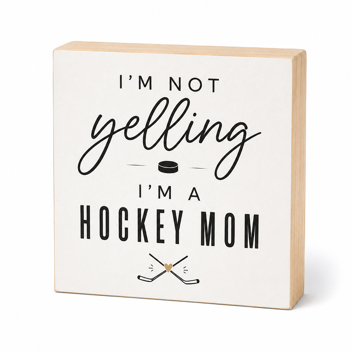 A square wooden block sign with a cream face and natural wood sides, printed with the phrase 'I'M NOT yelling I'M A HOCKEY MOM' in black lettering, along with a small hockey puck and crossed hockey sticks graphic, on a white background.