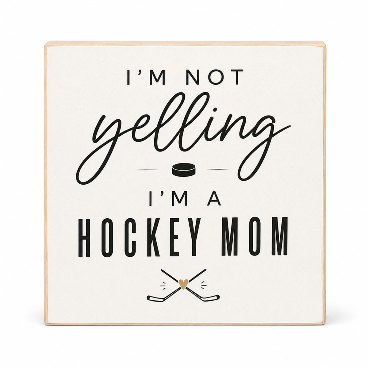 A square wooden sign with a light natural wood border and an off-white face, printed with the phrase 'I'M NOT yelling I'M A HOCKEY MOM' in black lettering, with a small hockey puck and crossed hockey sticks graphic.