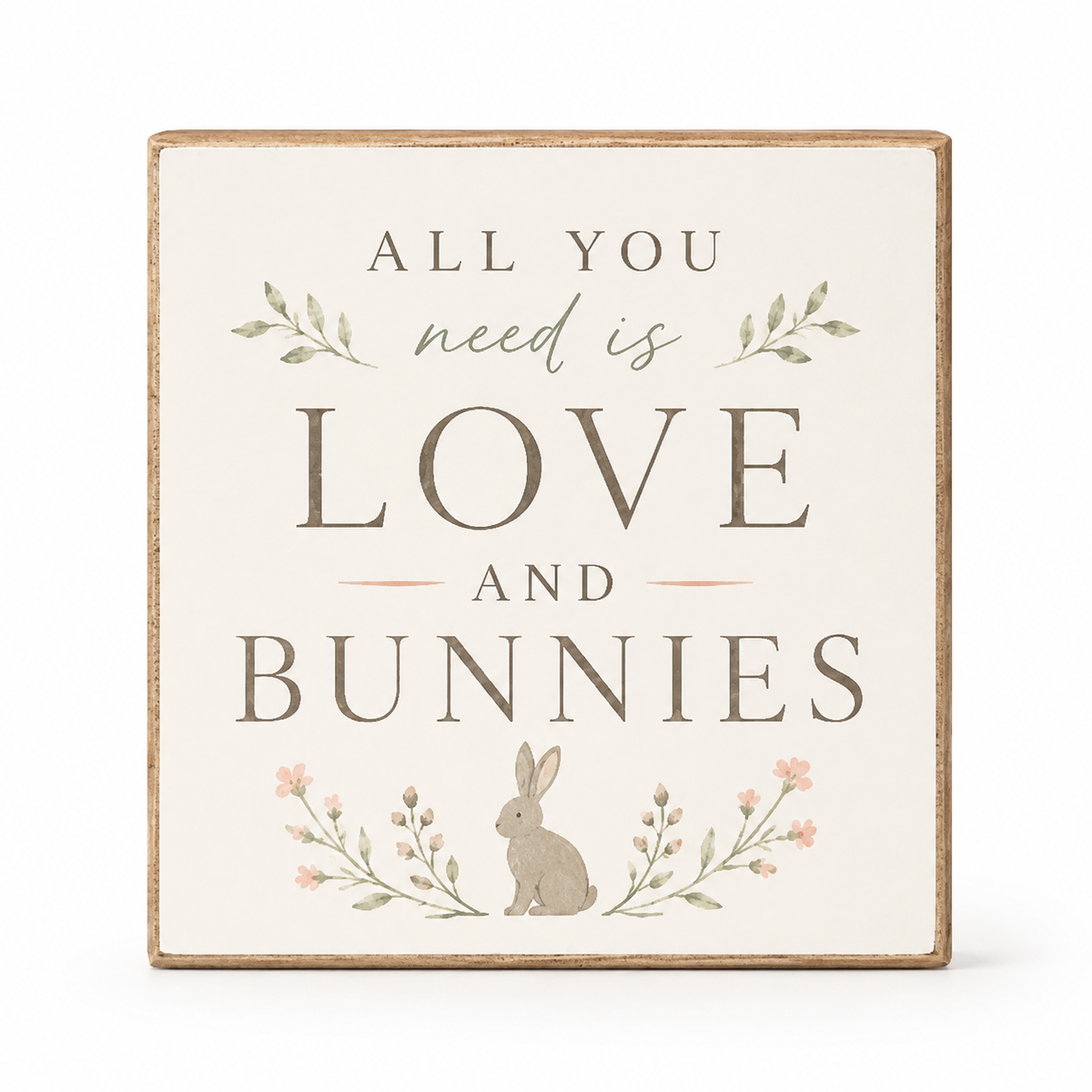 A square decorative wooden sign with a rustic light brown border, featuring the text 'ALL YOU need is LOVE AND BUNNIES' in muted brown and sage green lettering, with a small bunny illustration and floral details, shown on a white background.