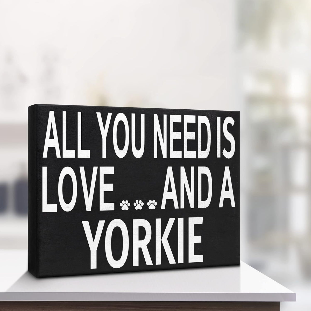 A rectangular black canvas wall sign with bold white text reading 'ALL YOU NEED IS LOVE.