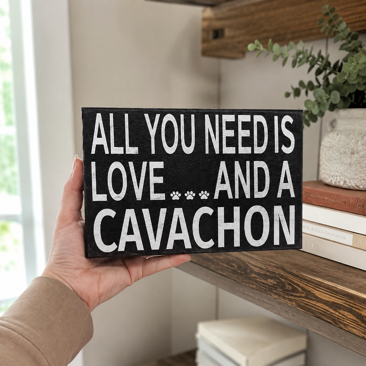 A hand holds a rectangular black sign with white text that reads 'ALL YOU NEED IS LOVE.