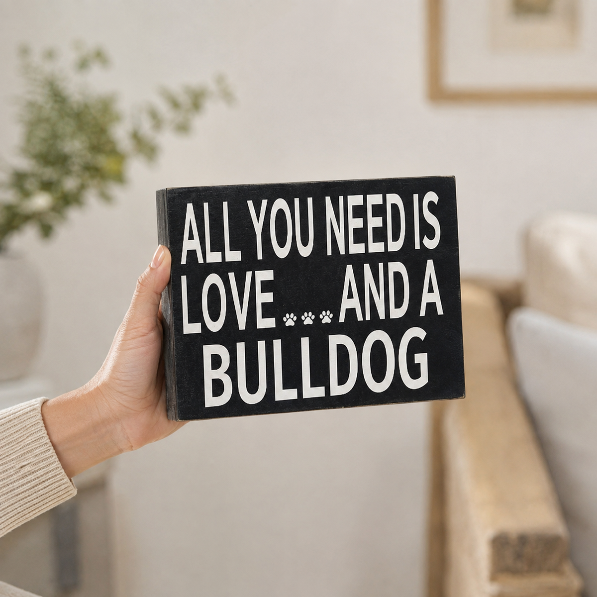 A hand holding a rectangular black sign with white text that reads 'ALL YOU NEED IS LOVE.