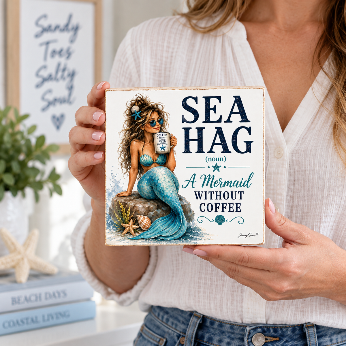 A woman holds a square decorative ceramic tile featuring an illustration of a mermaid with a blue tail and the text 'SEA HAG (noun) A Mermaid WITHOUT COFFEE'. The background shows a cozy, styled interior with books, a plant, and a framed sign.