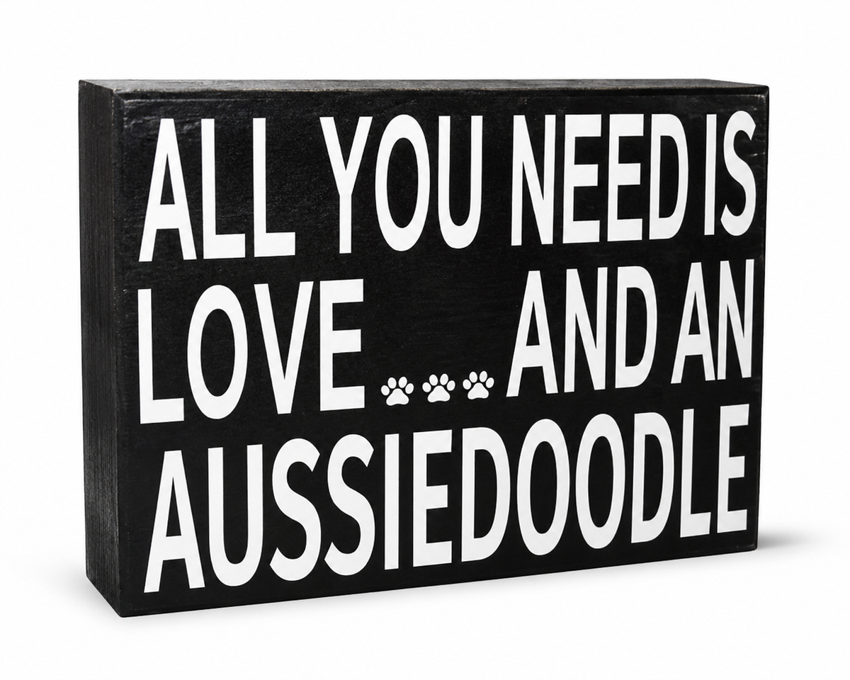 A rectangular black wooden sign with bold white text reading 'ALL YOU NEED IS LOVE.