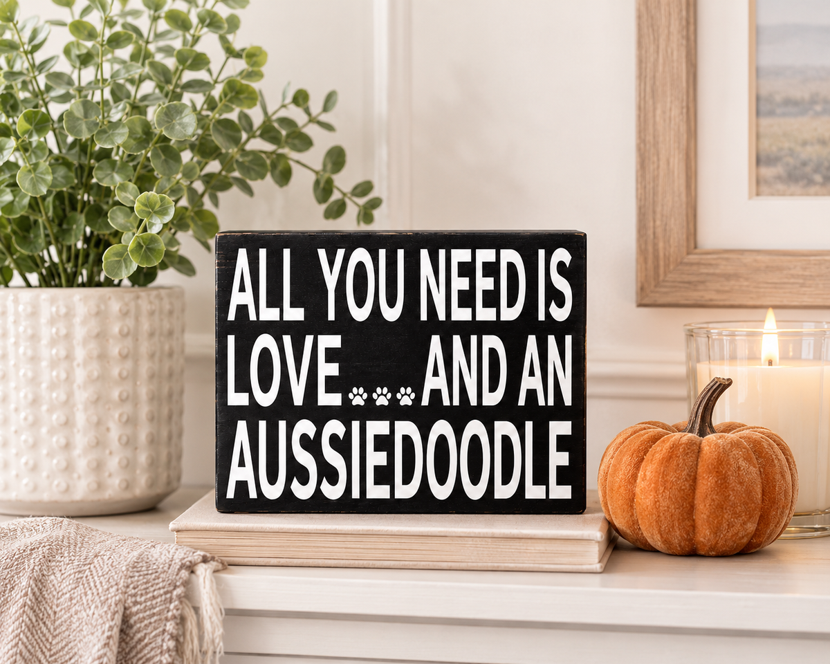 A rectangular black wooden sign with white painted text reading 'ALL YOU NEED IS LOVE.