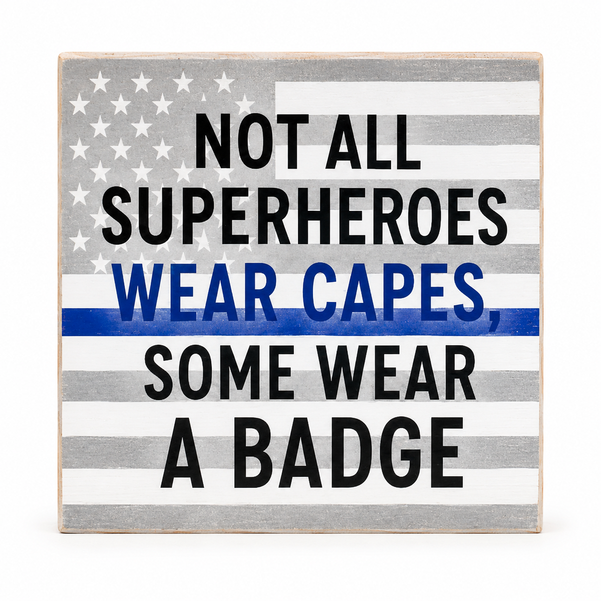 A square decorative sign with a distressed American flag design in gray, white, and black, featuring the text 'NOT ALL SUPERHEROES WEAR CAPES, SOME WEAR A BADGE' in black and blue lettering.