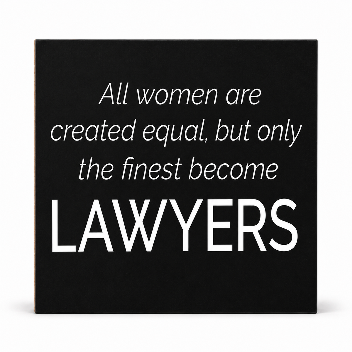 A square black decorative sign or canvas with white text reading, 'All women are created equal, but only the finest become LAWYERS,' shown against a light gray background.