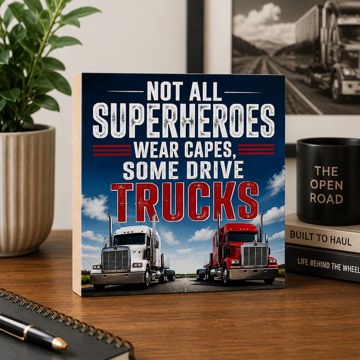 Book titled 'Not All Superheroes Wear Capes, Some Drive Trucks' on a desk with a truck-themed mug and plant.