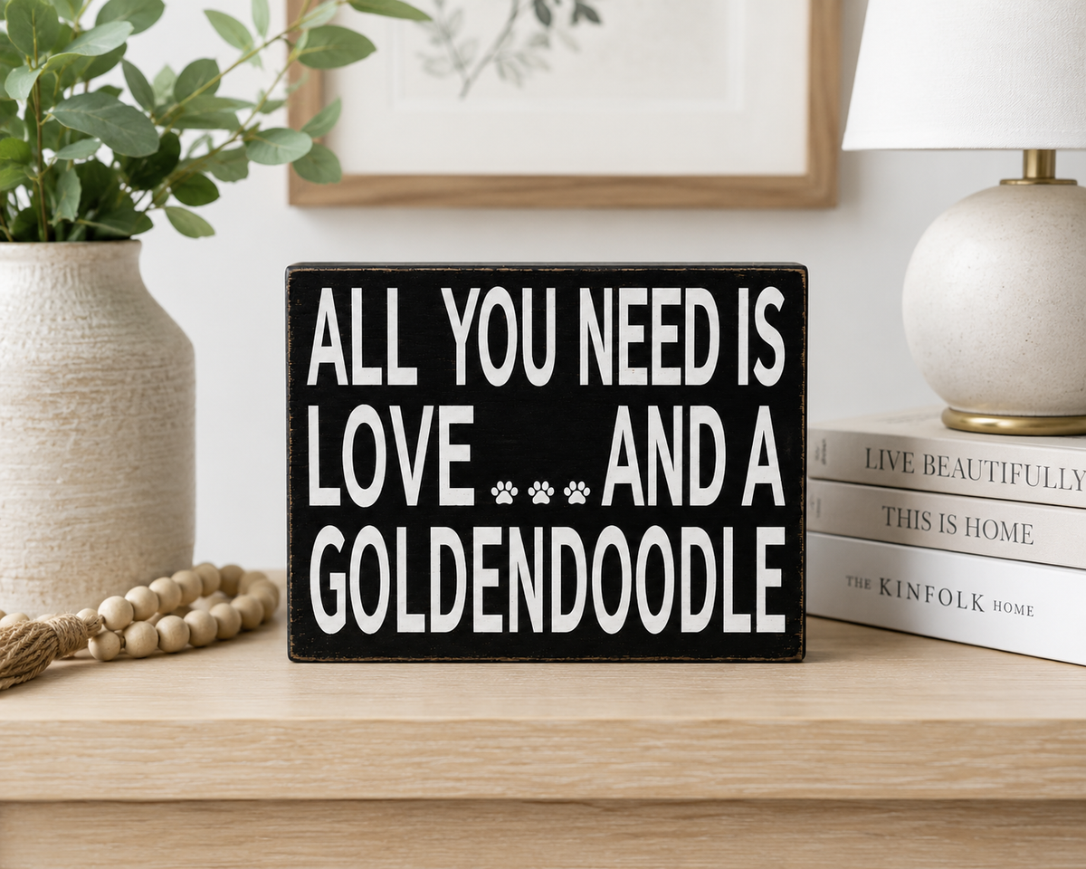 A rectangular black decorative sign with bold white text reading 'ALL YOU NEED IS LOVE.